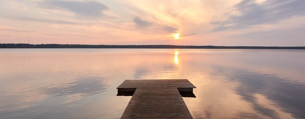 Busnieku lake at sunset. Ventspils, Latvia. Wooden pier. Soft sunlight, glowing clouds, symmetry...