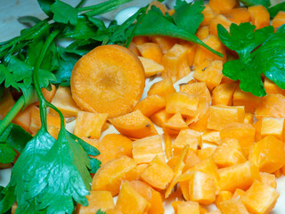 Finely chopped carrots and parsley leaves on the table. Cooking. Soup ingredients. Summer food. For a veggie lunch. Root crop on a cutting board.