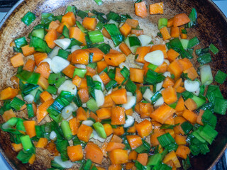 Carrots are fried in a pan along with leeks and garlic. Cooking food with smoke. Roasting vegetables.