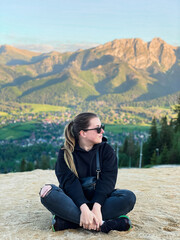 Fototapeta na wymiar Woman sitting on high hill with mountains on background during sunset
