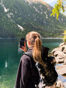 Young woman taking photos of mountain lake Morskie oko in Tatras