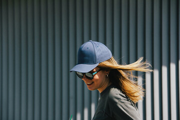 a girl in a cap and sunglasses smiles against a gray ribbed wall