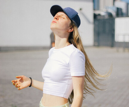 a girl with long hair in a cap and a white top raised her head