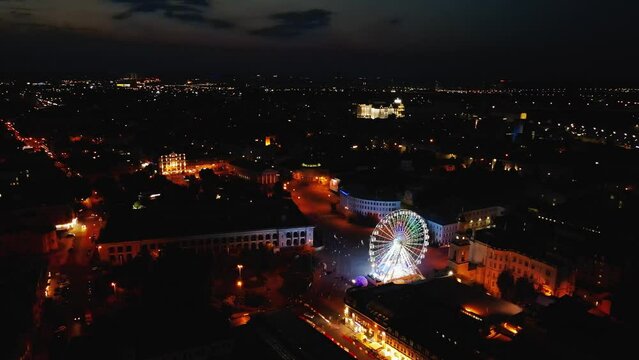 AERIAL: Kyiv City Downtown at night from above. Historical centre of the capital of Ukraine - Podil district, Ferris Wheel and Bridges in the background
