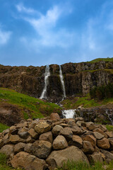 Pile of rocks in front of a waterfall that  formed from the melting mountain glacier during early summer near the town of Seydisfjordur in Iceland
