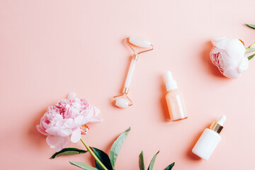 Dropper bottles with cosmetic oil, serum, facial roller and peony flowers on pink background. Top view, flat lay, copy space