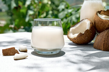 Coconut milk in glass and half of coconut on palm leaf background. Vegetable milk, lactose free non...