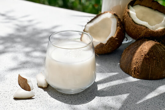 Coconut milk in glass and half of coconut on palm leaf background. Vegetable milk, lactose free non dairy healthy drink. Vegan food.