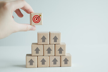 Hand holding dart board symbols on wooden block from top of stack. Business strategy, Action plan, Goal and target. Goal or agenda setting in business concept.