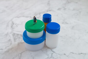 プラスチック容器と小瓶とミニチュア男ビジネスマンの中央配置の写真