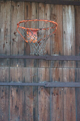 Ein Basketballkorb ist an ein Scheunentor montiert.  Die Farbe blättert ab. Beide sind sehr alt und abgenutzt, aber sie funktionieren noch. Das Scheunentor ist aus Holz und hat eiserne Beschläge.