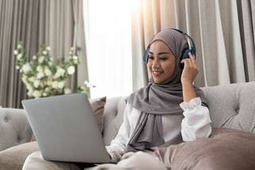 Asian muslim woman having video teleconference on her laptop at home, online learning or working...