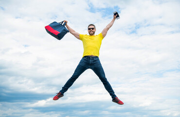 Fototapeta na wymiar Active man jumping with travel bag midair sky background, vacation