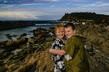 Boys wearing hooded towels after swimming mucking around on rocks at The Tanks tourist attraction at Forster, NSW Australia