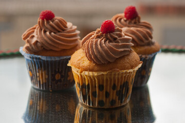 Beige cupcakes made of delicate light sponge cake decorated with chocolate cream. Topped with ripe raspberries.