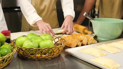 Close-up at hands of chef in cook uniform with apron, cooking class students stuff ingredients in pastry dough and pressing for bakery foods, prepare fruit pies in restaurant stainless steel kitchen.