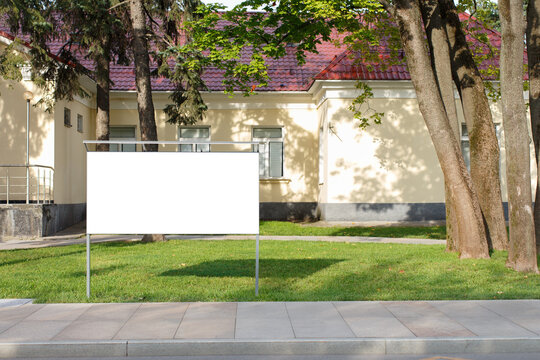 Horizontal information board on a lawn against the background of a one-story house with a red roof.