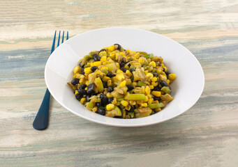 Cooked black beans, corn, and zucchini  vegetable side dish or ingredient or filing in white bowl with blue fork