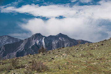 Mountain range under blue sky with cumulus clouds. Rocks and cliffs on horizon on sunny day. Travel through highlands on foot.