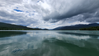 Whitefish Lake in Flathead County, Montana under dramatic summer cloudscape reflected in calm water of lake.