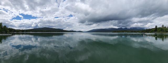 Whitefish Lake in Flathead County, Montana under dramatic summer cloudscape reflected in calm water of lake.