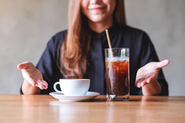 Closeup image of a young woman make presenting hands to two glasses of iced coffee and hot coffee