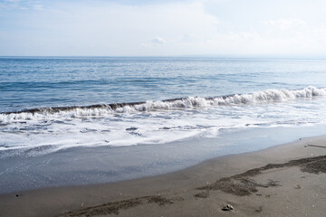 Small waves ripple on the black sandy beach.