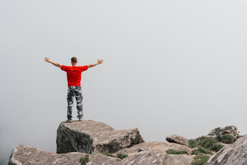 Hiker man on the top of the mountain enjoys the aerial view, raising his hands above the clouds. Mount Pidan