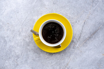 A cup of coffee photographed flat lay on a yellow cup saucer.