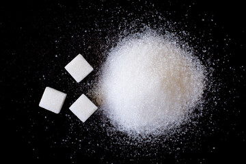 Pile of white sand sugar and sugar cubes isolated on dark background, top view, flat lay. 