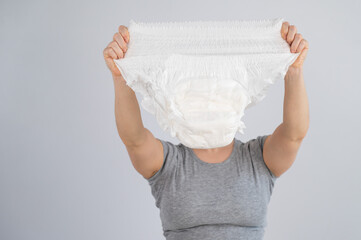 A caucasian woman holds an adult diaper and checks its strength on a white background. 