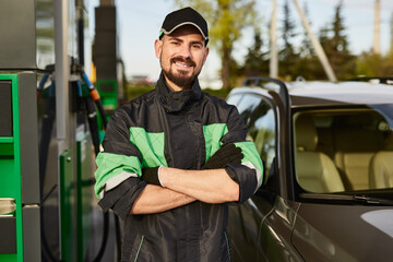 Smiling man standing at filling station near modern car during work