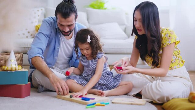 Happiness Family sitting in casual living room playing moulds from plasticine at home, Girl daughter sculpt figures from soft colorful  Clay Dough with her parents with joyful smile watching takecare