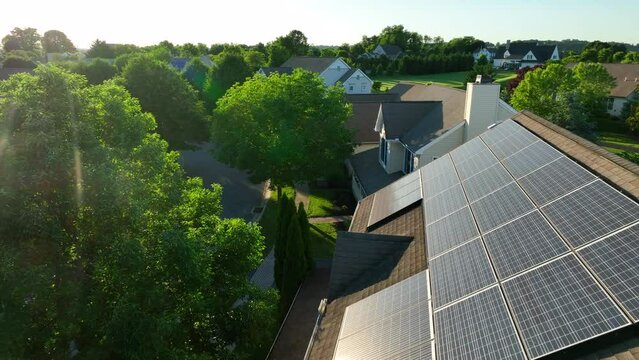 Rooftop solar panels on home in American neighborhood. Sun reflects light. Green renewable energy theme. Aerial.