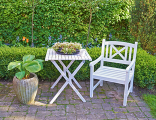 White wooden chair and table in a green garden with blossoming plants and copyspace. Tranquil landscape to relax and enjoy a cosy picnic in summertime. Outdoor patio in a quiet and secluded courtyard