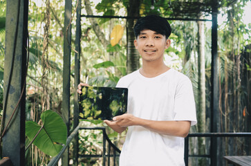 smiling asian man showing tablet screen on nature background