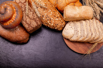 Top view of sliced wholegrain bread on dark ructic wooden background closeup. Various tasty rolls and breads with grains . White and rye bread, buns with copy place. Composition with bread and rolls.