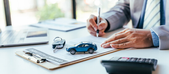 Man signing car insurance document or lease paper. Writing signature on contract or agreement. Buying or selling new or used vehicle. Car keys on table. Warranty or guarantee. Customer or salesman. - obrazy, fototapety, plakaty