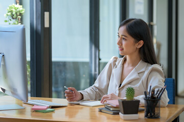 Asian businesswoman sitting happily working on her laptop in the office.