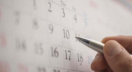 Hand holding a pen and pointing with finger to a monthly calendar
