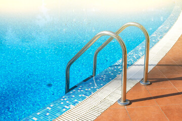 Fototapeta na wymiar Stainless ladder and handrails in outdoors swimming pool on summer sunny day. Seaside vacation and hotel resort concept. Entrance in blue clean sea water pool