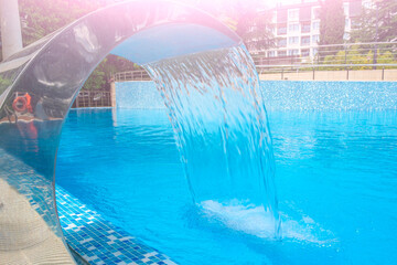 Pool side. Empty outdoors swimming pool and waterfall jet on summer sunny day. Seaside vacation and hotel resort concept. Reflection in blue clean sea water pool