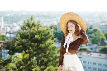 Portrait of a beautiful young girl in a straw hat, posing against the background of the city from an observation deck.