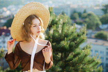 Portrait of sweet blonde girl in straw hat posing on a background of the city.