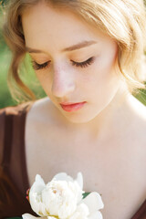 Obraz na płótnie Canvas Close-up portrait of a cute blonde with a white flower in her hand. Soft blur background