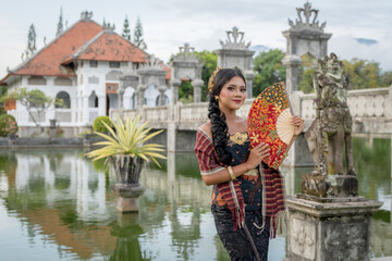 Portrait young asia girl with balinese traditional clothes standing in front of the garden bridge