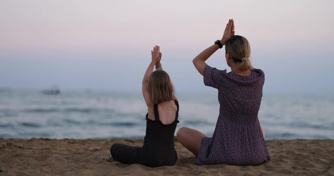 Silhouette of mother and daughter doing yoga by sea on beach