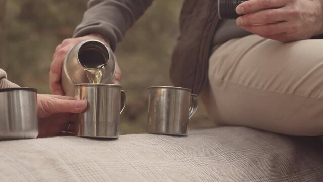 Slowmo closeup of unrecognizable couple drinking hot tea from stainless steel thermos cups in forest