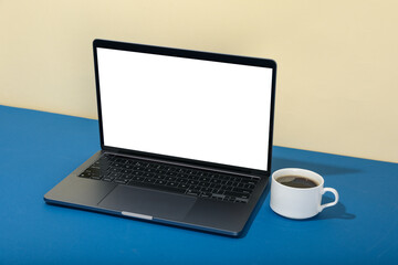 Fototapeta premium Laptop with blank screen and cup of coffee on two tone background