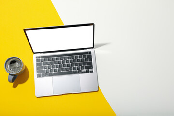 Laptop with blank screen and cup of coffee on two tone background